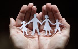 Pair of hands holding a paper family of daughter, father, mother, son