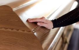 Photo of a womans hand touching a brown casket.