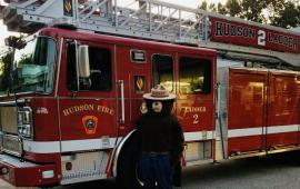 Photo of Ladder 2 - red fire truck with ladder across truck.  Smokey the Bear standing next to the drivers door.