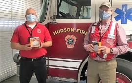 Two men holding smoke alarms in front of a fire truck