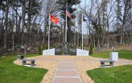 View of the three part memorial composed of granite & marble with flags and trees in background.