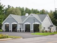 4 Black windowed apparatus bay doors on a grey building with two peaks and white trim