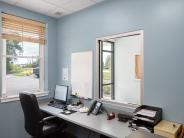 Blue walled room with a window on the left and a desk to the right with a window above it