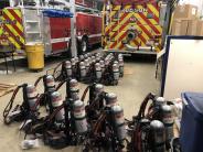 Photo of several SCBA packs on a concrete floor.  Grey cylinders in a black strapped holder
