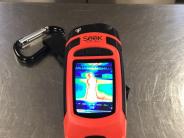 Orange handheld thermal imaging camera.  Display shows various colors of heat.