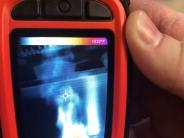 Orange handheld thermal imaging camera.  Display shows various colors of heat.