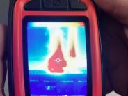 Orange handheld thermal imaging camera.  Display shows various colors of heat.