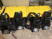 Oxygen tank holders - Image of several black backpack like units against yellow covered bins.