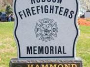 Granite stone reading Hudson Firefighters Memorial with last alarm logo in middle sitting on a marble stone.