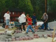 Photo of several people laying bricks and a young boy rolling a roller leveling concrete.