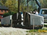 A crane hoisting a three part concrete memorial into place.