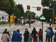 Group of people standing watching a parade of members and apparatus approach the memorial.