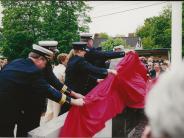 Several firefighters dressed in their Class A, pulling up a red cloth from off the memorial.