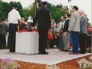Photo of several people gathered around the memorial bell which was atop a granite pillar.