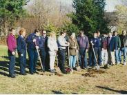 15 men and woman lined up with shovels in hand for a ground breaking ceremony of the new memorial.
