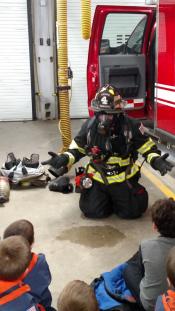 Firefighter dressed in protective gear showing children the different equipment they use.