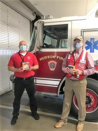 Two men holding smoke alarms in front of a fire truck