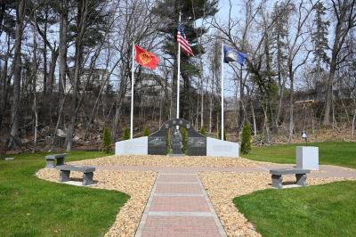 View of the three part memorial composed of granite & marble with flags and trees in background.