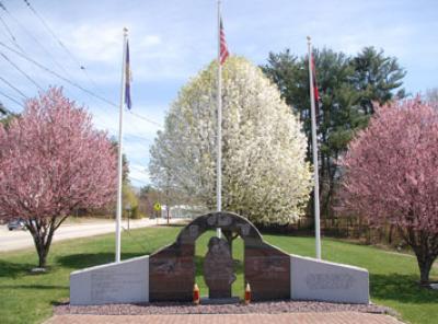 View of the three part memorial composed of granite & marble with flags and flowering trees in background.